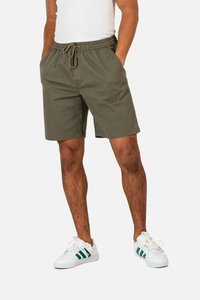 Olive green shorts with an elastic waistband and drawstring, featuring side pockets and a relaxed fit, paired with white sneakers.
