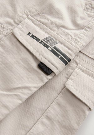 Tessuto beige chiaro con una sottile trama a righe, dotato di un'etichetta con testo nero e un codice a barre, e un accento in tessuto nero.