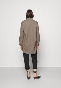 Brun, ullblandad kappa med hög krage och långa ärmar, med rak skärning och knappdetaljer. Matcher med svarta cropped byxor och klackar.