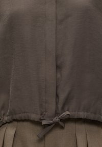 Tissu brun noué en nœud sur un tissu beige plissé, montrant les coutures détaillées et la texture des matériaux.