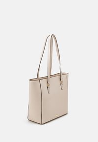 Béžová kožená taška s dlouhými uchy, kontrastním černým lemem a minimalistickým designem. Obsahuje akcent v zlatém tónu s logem.