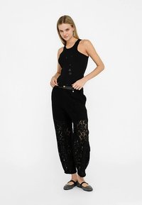 Sort tanktop parret med sorte blondebukser med løs pasform, tekstureret blondeoverlay og et dekorativt bælte med metalaccenter.