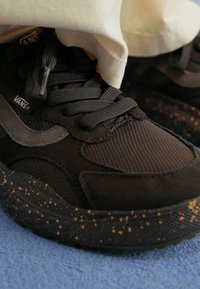 Sapatilhas pretas feitas de malha e camurça, com parte superior texturizada, fecho de atacadores e sola salpicada de preto e amarelo.