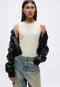 Γκρι αμάνικο τοπ με λογότυπο, υπερμεγέθη μαύρο δερμάτινο μπουφάν και ανοιχτό μπλε ξεθωριασμένο τζιν με χαλαρή εφαρμογή και ίσια γραμμή.