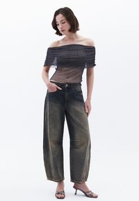 Off-the-shoulder gennemsigtig bluse med tekstureret mønster, parret med højtaljede, løst fit, falmede denimjeans og snørede hæle-sandaler.