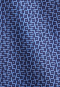 Tissu bleu avec un motif répétitif de formes florales à quatre pétales entrelacées bleu foncé sur un fond bleu plus clair.