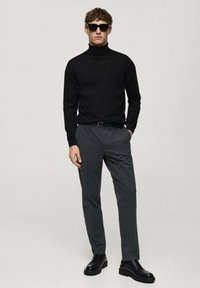 Schwarzer Rollkragenpullover, graue maßgeschneiderte Hose, schwarze Schuhe und Sonnenbrille. Glatte Texturen und schmale Passform, minimalistischer Stil.