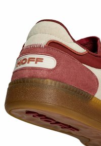 Primer plano de un talón de zapatilla de gamuza rosa y beig con una suela marrón texturizada y el logo "HOFF" en un parche de goma blanca.