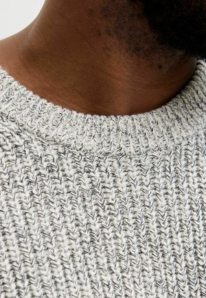 Grå strikket sweater med et struktureret mønster og en ribbet halskrave. Stoffet ser blødt ud og har en subtil meleret effekt.