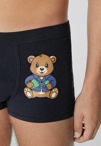 Černé boxerky s velkým kresleným medvědím motivem. Medvěd je zobrazen ve modré bundě, jak drží peníze. Měkká, pružná tkanina.