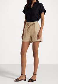 Black short-sleeve button-up shirt paired with beige high-waisted shorts featuring a tied waist. Worn with black strappy sandals.