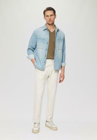 Jasnoniebieska koszula dżinsowa, oliwkowa koszulka z dekoltem w serek, białe spodnie i beżowe sneakersy. Dżins ma klasyczny kołnierzyk i dwie kieszenie na piersi.