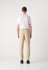 Beige teksturerte bukser med avslappet passform, parret med en hvit t-skjorte. Bakvisningen viser to baklommer og elegante svarte sko.
