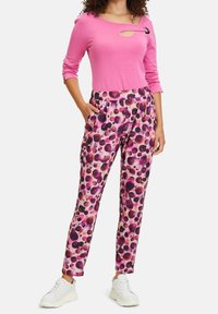 Pink long-sleeve top with a cutout and black accent, paired with colorful, patterned pants featuring pink, purple, and black dots. White sneakers.