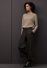 Beżowy lekki sweter o luźnym kroju, zestawiony z ciemnymi, szerokimi spodniami w paski. Błyszczące czarne botki z złotymi akcentami.