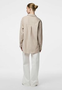 Camicia a righe beige chiaro con maniche lunghe, piega sul retro e colletto, abbinata a pantaloni bianchi a gamba larga. Tessuto con texture liscia.