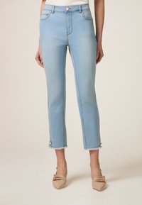 Jeans de mezclilla azul claro con corte ajustado, longitud recortada, detalle de dobladillo sin terminar y bolsillos frontales; combinados con zapatos nude de punta afilada.
