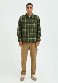Grün-beige karierter Flanellhemd mit zwei Brusttaschen, Knopfverschluss, kombiniert mit beigen Cargo-Hosen und grauen Sneakers.