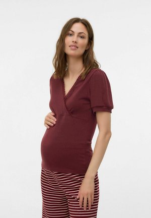 Maglia da maternità in tessuto ribbed bordeaux con scollatura a V e maniche corte a palloncino. Abbinata a pantaloni a righe bordeaux e bianchi.