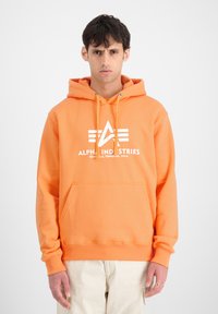 Sudadera naranja hecha de material suave, con un bolsillo frontal, capucha con cordón y un logo blanco con diseño geométrico en el pecho.