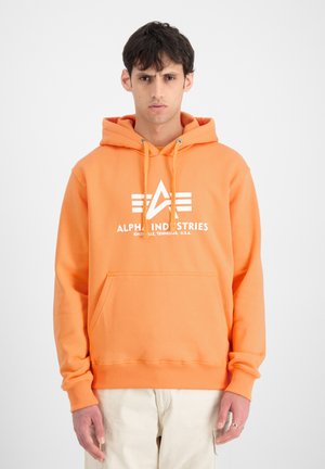 Felpa arancione realizzata in materiale morbido, con tasca frontale, cappuccio regolabile e logo bianco con design geometrico sul petto.