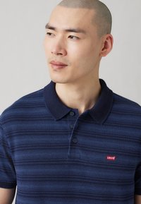 Tricou polo albastru marin cu dungi orizontale, guler cu trei butoane și logo-ul Levi's roșu pe piept. Material moale cu un design cu guler.
