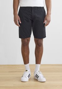 Shorts noirs en mélange de coton, avec des poches avant et une coupe droite, associés à des chaussettes blanches et des baskets blanches à rayures noires.