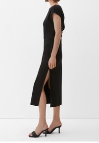 Black midi dress with a fitted silhouette, short sleeves, side slits, and smooth texture. Worn with black heeled sandals.