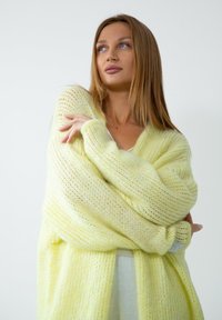 Jasnożółty sweter dzianinowy z otwartym przodem, długimi rękawami i luźnym krojem. Miękka tekstura oraz przytulny, przewiewny wygląd.
