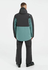 Herrejakke med en sort overdel og en teal nederdel, samt hætte og manchetter. Bæres med mørke bukser og skistøvler.