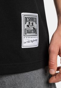 Black t-shirt featuring a prominent white label with gray text and stars. Fabric appears smooth with a relaxed fit.