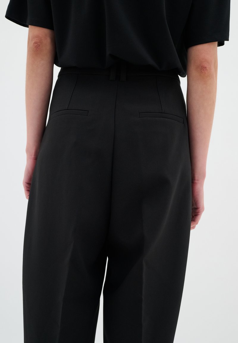 Schwarze hoch taillierte Hose mit glatter Textur, ausgestattet mit zwei Gesäßtaschen, dezenten Nähten und einem geraden Schnitt.