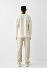 Ljusbeige långärmad skjorta och matchande byxor, tillverkade av mjukt tyg. Enkel design med avslappnad passform och inga framträdande detaljer.