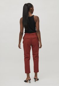 Pantalon rouge fuselé avec une ceinture élastique et des poches arrière, assorti à un haut noir sans manches et des mules noires à talons.