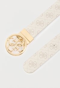 Beigen sävyinen kuvioitu kangasvyö, jossa on sileä kultainen pyöreä solki, jossa on toisiinsa kietoutuneet kirjaimet. Hihnassa on hienovarainen tekstuuri ja pyöristetty pää.