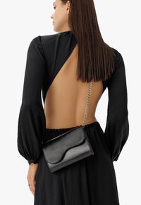 Borsa a tracolla in pelle nera con motivo a onde sulla parte anteriore, tracolla in catena argento e forma rettangolare compatta. Texture liscia.