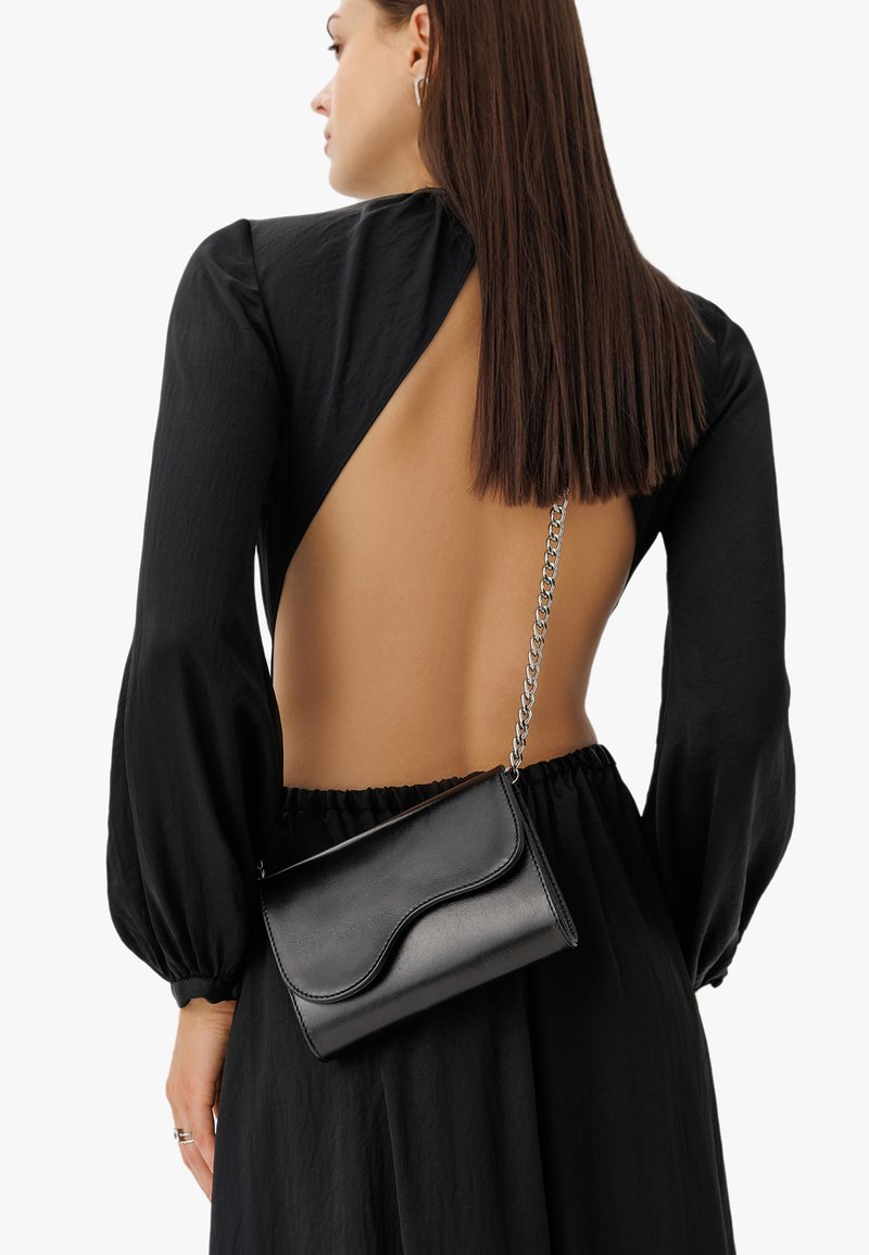 Borsa a tracolla in pelle nera con motivo a onde sulla parte anteriore, tracolla in catena argento e forma rettangolare compatta. Texture liscia.