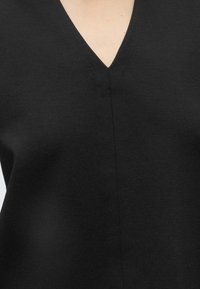 Gros plan d'un vêtement noir à col en V montrant une texture lisse du tissu et le détail de la couture centrale au niveau de la poitrine haute.