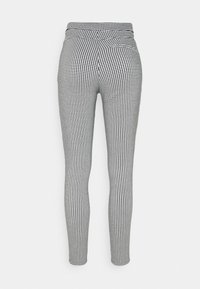Pantalon taille haute slim fit avec petit motif pied-de-poule noir et blanc, vue de dos sur fond clair uni.