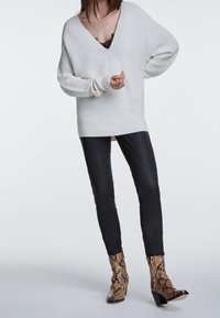 Maglione bianco a V con maniche larghe, abbinato a pantaloni in ecopelle nera e stivaletti con tacco a blocco e motivo a serpente.