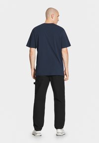 Granatowa bawełniana koszulka z krótkim rękawem, okrągłym dekoltem i luźnym krojem, w połączeniu z czarnymi spodniami i białymi trampkami.