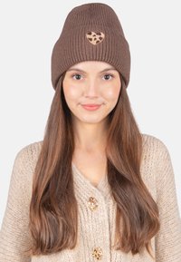 Braune gerippte Strickmütze mit einem Herz-Patch im Leopardenmuster, kombiniert mit einer beigen gestrickten Strickjacke mit goldfarbenen Knöpfen.