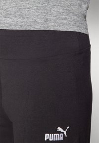Čierne športové legíny vyrobené z elastického materiálu, s hladkým povrchom a bielym logom Puma na ľavej strane.