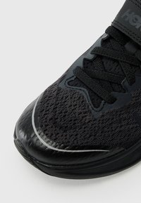 Baskets de sport noires avec un dessus en maille texturée, fermeture à lacets et accents synthétiques brillants. Semelle incurvée avec un détail réfléchissant.