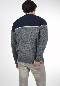 Jersey de punto con una sección superior de color azul marino y una franja de acento blanca, y una sección inferior gris texturizada, combinado con jeans gris claro.