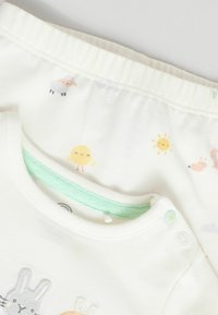 Ensemble pour bébé en coton blanc comprenant un haut à manches courtes avec des broderies d'animaux et un pantalon de pyjama doux à motifs avec une taille verte.