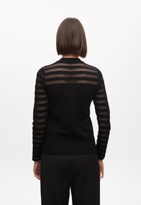 Čierny top s dlhými rukávmi a priesvitnými pruhovanými rukávmi, s pevným telom. Má okrúhly výstrih a priliehavý strih, v kombinácii s čiernymi plisovanými nohavicami.