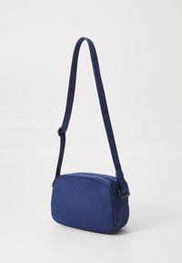 Borsa a spalla di tessuto blu con forma rettangolare, dotata di una tracolla con marchio e chiusura con cerniera. Texture liscia con materiale resistente.