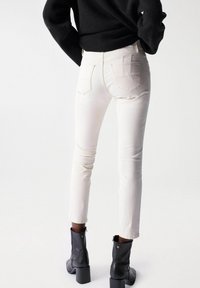 White jeans with a slim fit and subtle pocket detailing, paired with black ankle boots featuring a chunky heel and smooth leather texture.