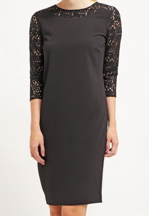 Robe noire avec des manches en dentelle trois-quarts, silhouette ajustée, encolure ronde et textile lisse. La dentelle présente un motif complexe.